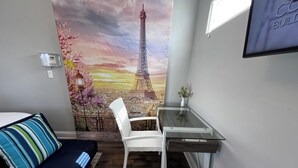 Ein Zimmer mit einem Bett, einem weißen Stuhl, einem Schreibtisch, einem Wandbild des Eiffelturms und einem Fenster.