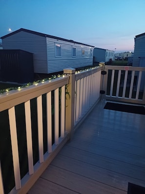 A deck with a white railing, a gated entrance, and a row of mobile homes in the background. - Family Caravan-pets-golden Palm-pool-arcades (Skegness)