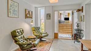 Ein geräumiges Wohnzimmer mit zwei grünen Ledersesseln, einem Holztisch und einem großen Fenster mit Blick ins Freie.