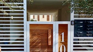 A modern building entrance with a wooden door marked '10', a stone wall, and a metal gate with mailboxes. - GuestHost - Brand New Apartment with Pool and Terrace - Two Steps from the Beaches (Palau)