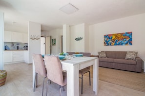 A modern living room with a dining table, chairs, a sofa, and a painting on the wall.