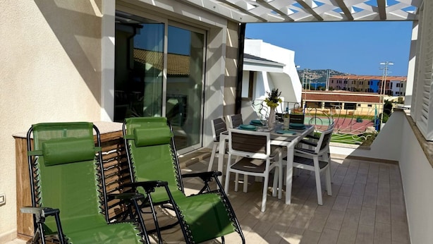 A balcony with green chairs, a table, and a view of buildings and a beach. - GuestHost - Brand New Apartment with Pool and Terrace - Two Steps from the Beaches (Palau)