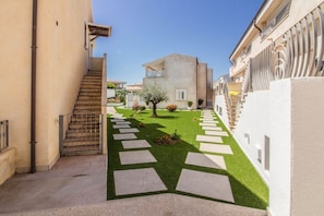 A narrow courtyard with a staircase, a tree, and a building with balconies.