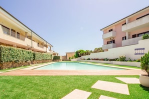 A swimming pool surrounded by a well-maintained lawn and a building with balconies.