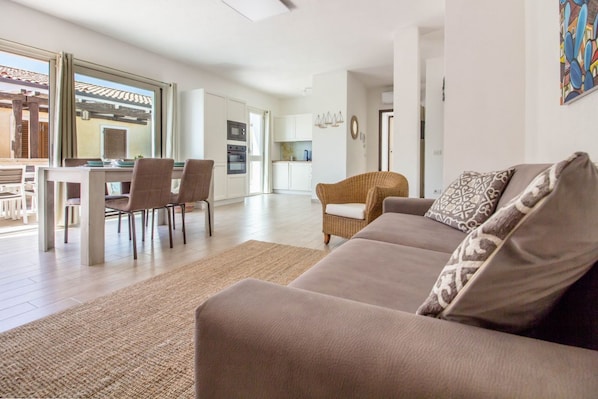 A living room with a sofa, chairs, a dining table, and a kitchen in the background.