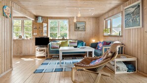 Une pièce chaleureuse, avec des murs en bois, un canapé, un fauteuil à bascule, une télévision et une fenêtre donnant sur des immeubles.