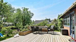 Une terrasse en bois avec des meubles d’extérieur, un espace de jeux et un jardin.