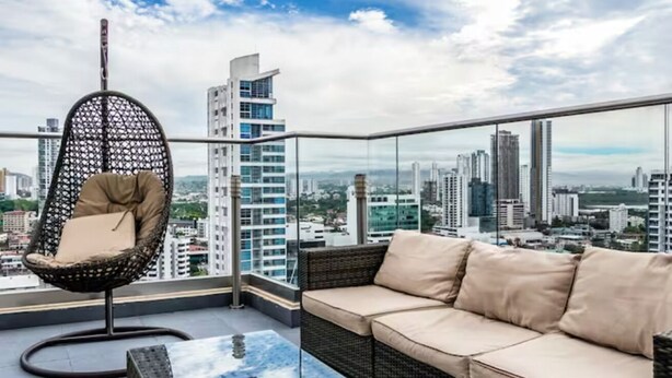 Ein Balkon mit Korbstuhl und Sofa, mit Blick auf die Stadt.
