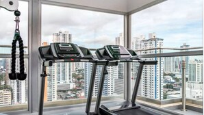 Ein Fitnessstudio mit Laufbändern und Kraftgeräten, große Fenster mit Blick auf die Stadt.