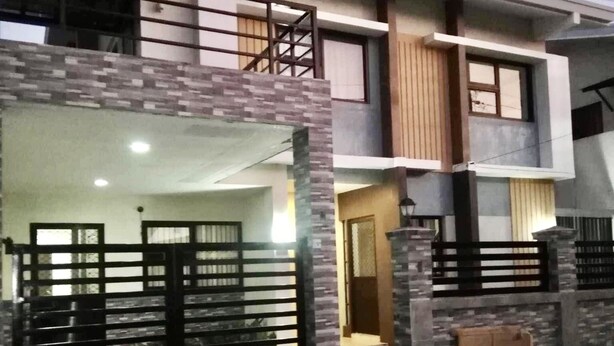 A two-story residential building with a balcony, a gated entrance, and a visible trash bin.