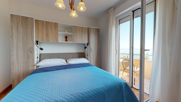 Una camera da letto con un letto, un comodino, un armadio a muro e una porta vetrata scorrevole che dà su un balcone con mobili da esterno.
