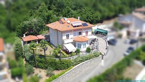 Una casa a due piani con tetto in tegole rosse, un balcone e un giardino con palme.