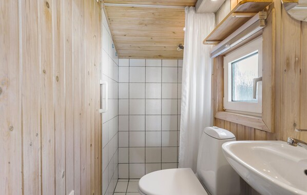 Un baño con paneles de madera, que incluye inodoro, lavamanos y zona de ducha.