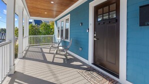 A covered porch with a wooden ceiling, a blue exterior wall, and a dark brown door. - Home Away From Home in Lowell (Lowell)