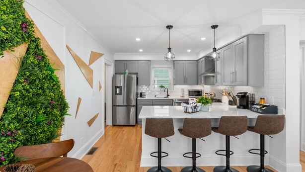 A modern kitchen with a central island, bar stools, stainless steel appliances, and a green vertical garden. - Home Away From Home in Lowell (Lowell)