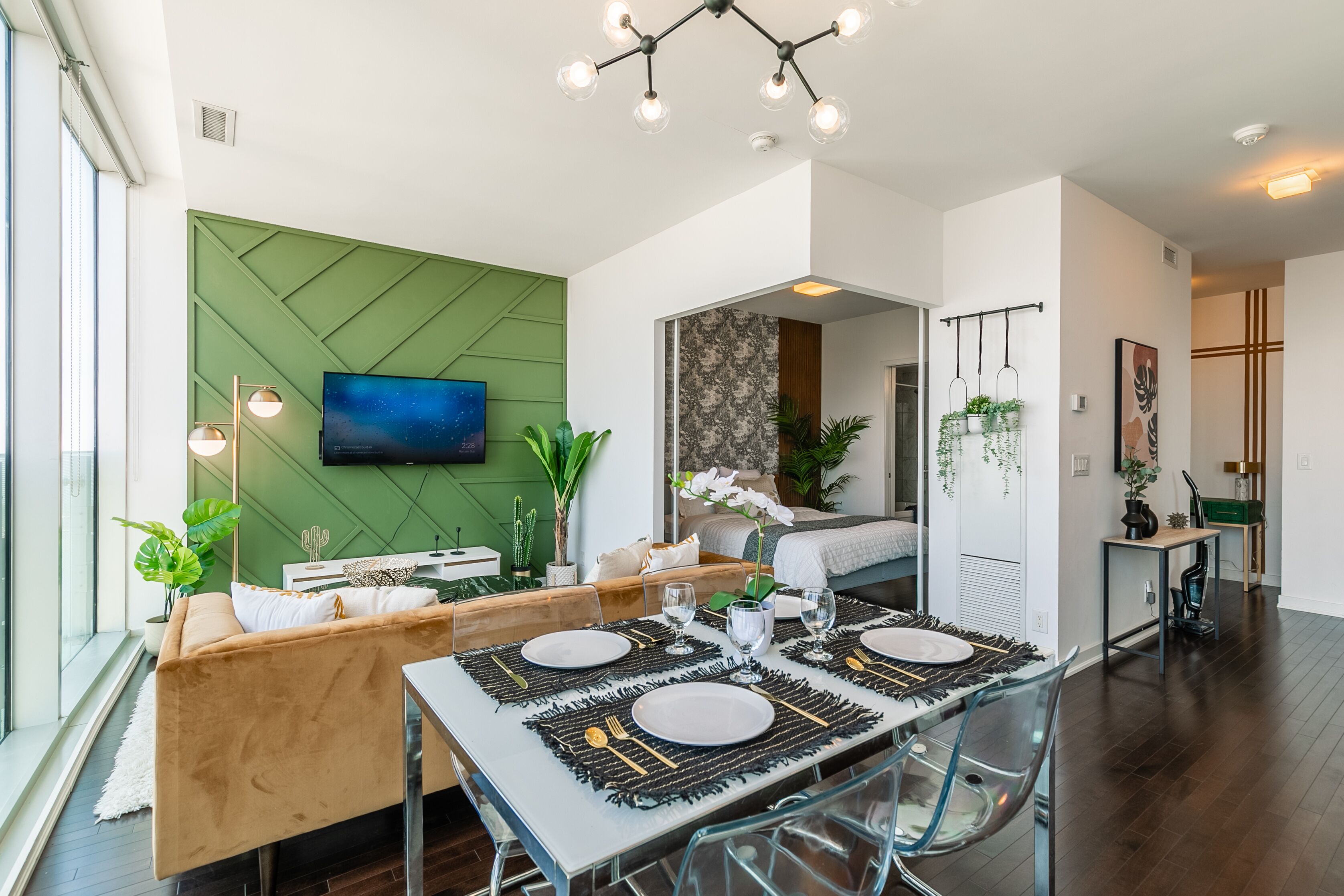 A modern dining area with a green accent wall, a flat-screen TV, and a dining table set for four.