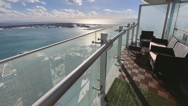 A balcony with a glass railing overlooking a body of water and a distant shoreline. - SkyTree Modern Suites (Toronto)