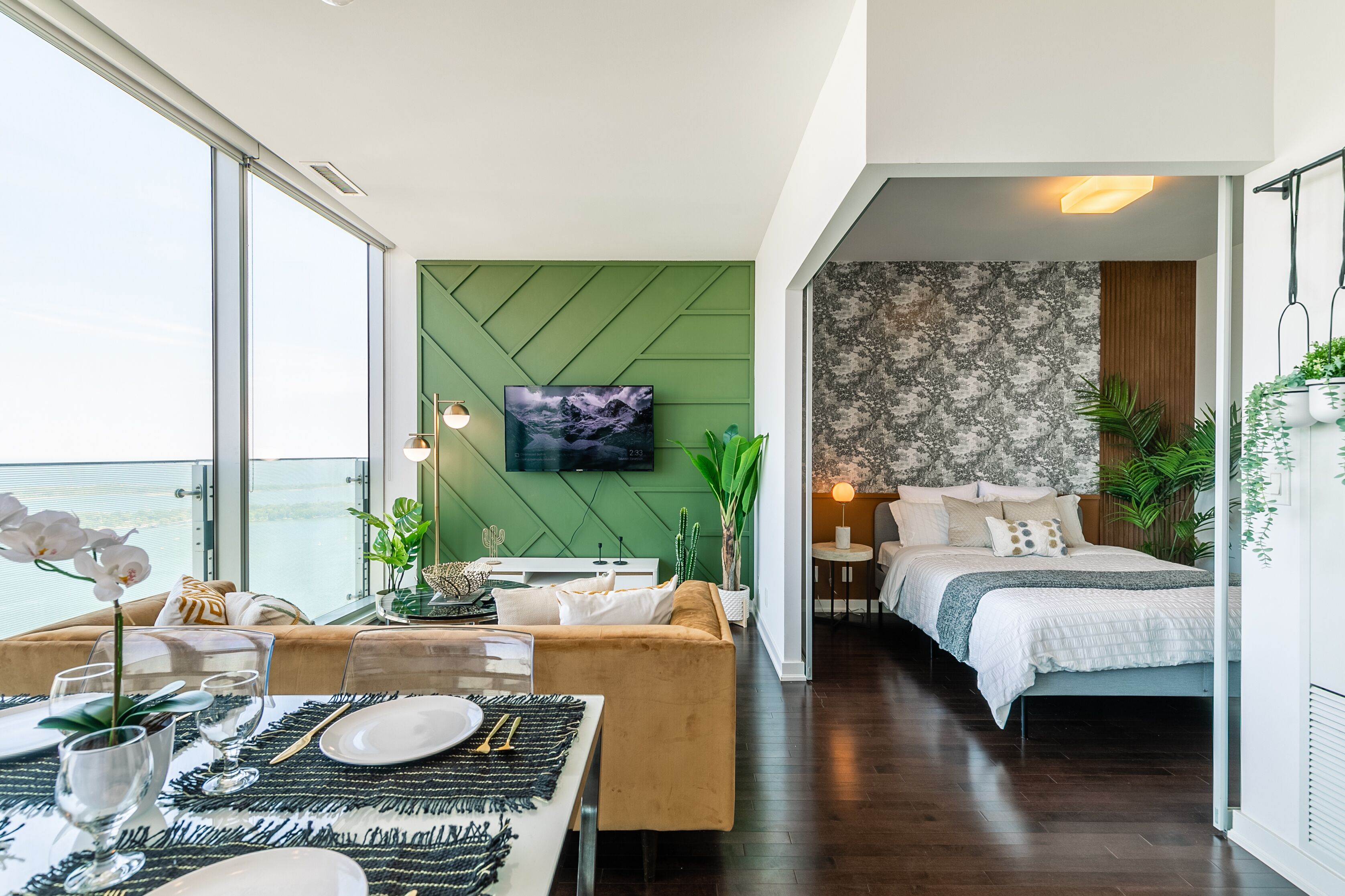 Una habitación de hotel moderna con área de comedor, cama con vistas y pared verde decorativa.