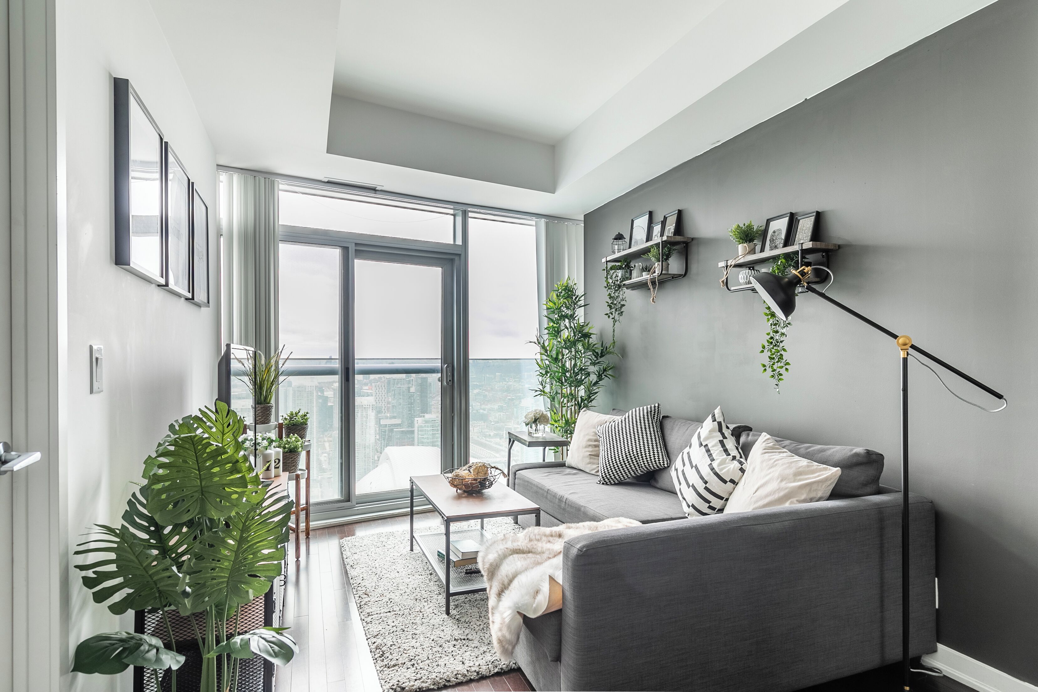 Un salon moderne avec un canapé gris, une table basse et une grande fenêtre donnant sur la ville.