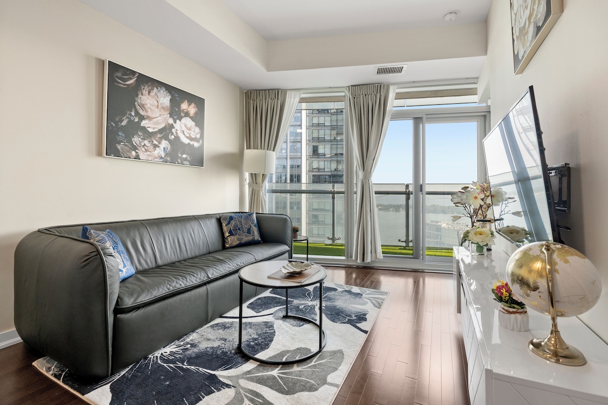 A modern living room with a leather sofa, a round coffee table, and a large window with a view of a building and greenery.
