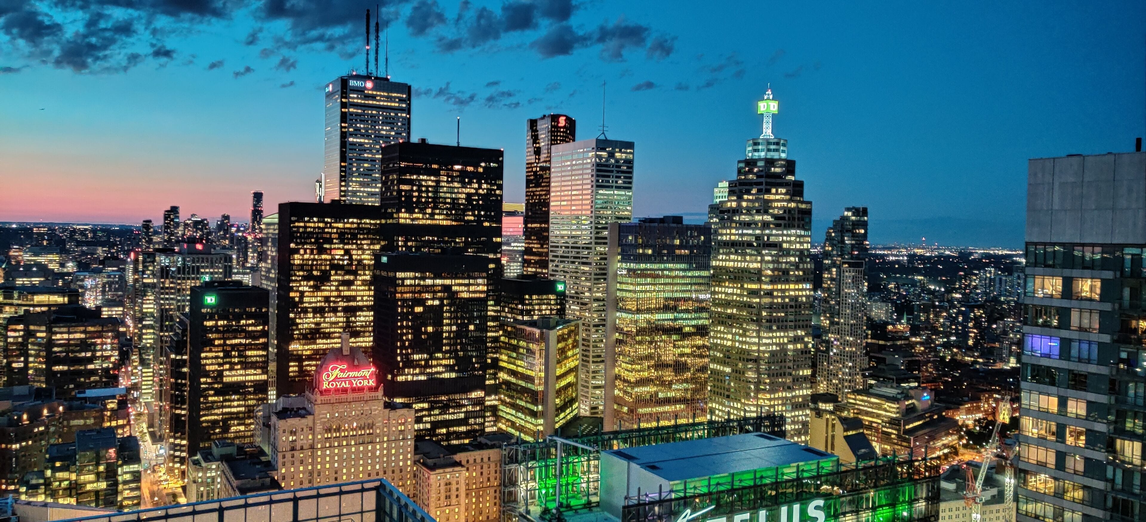 Un horizonte urbano con edificios iluminados, incluyendo un hotel destacado con un letrero verde.