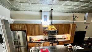 A modern kitchen with wooden cabinets, stainless steel appliances, a central island with bar stools, and a hanging pendant light. - Beautiful High-End 4 Bed 3 Bath House, Sleeps 15! (Pittsburgh)
