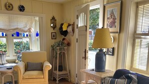 A cozy living room with a sofa, armchair, and a coffee table. There is a door leading outside, and the room has a tiled floor. - Charming Cottage in Carmel-by-the-Sea. Blocks from downtown and the beach! (Carmel-by-the-Sea)