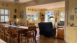 A dining area with a wooden table and chairs, a blue armchair, and a kitchen area with a cabinet and a lamp. - Charming Cottage in Carmel-by-the-Sea. Blocks from downtown and the beach! (Carmel-by-the-Sea)