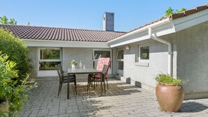 A patio with a table and chairs, a large potted plant, and a building with a tiled roof and windows. - Cozy home in Slagelse with WiFi (Slagelse)