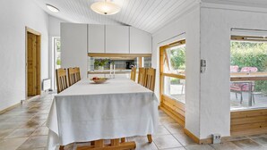 A dining area with a long table, wooden chairs, a white tablecloth, and a view of the outdoors through large windows. - Cozy home in Slagelse with WiFi (Slagelse)