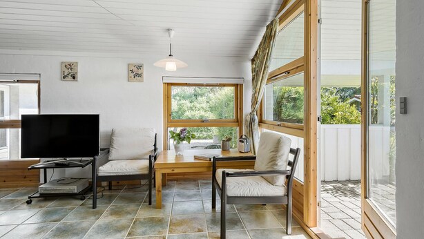 A cozy living room with a TV, two chairs, a table, and a large window offering a view of greenery. - Cozy home in Slagelse with WiFi (Slagelse)