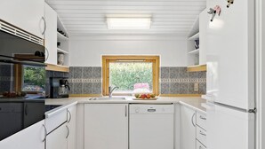 A modern kitchen with white cabinetry, a Bosch dishwasher, a window with a view of greenery, and a countertop with fruits. - Cozy home in Slagelse with WiFi (Slagelse)