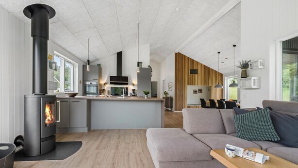 A modern kitchen with a central island, a built-in stove, and a dining area with a wooden accent wall.