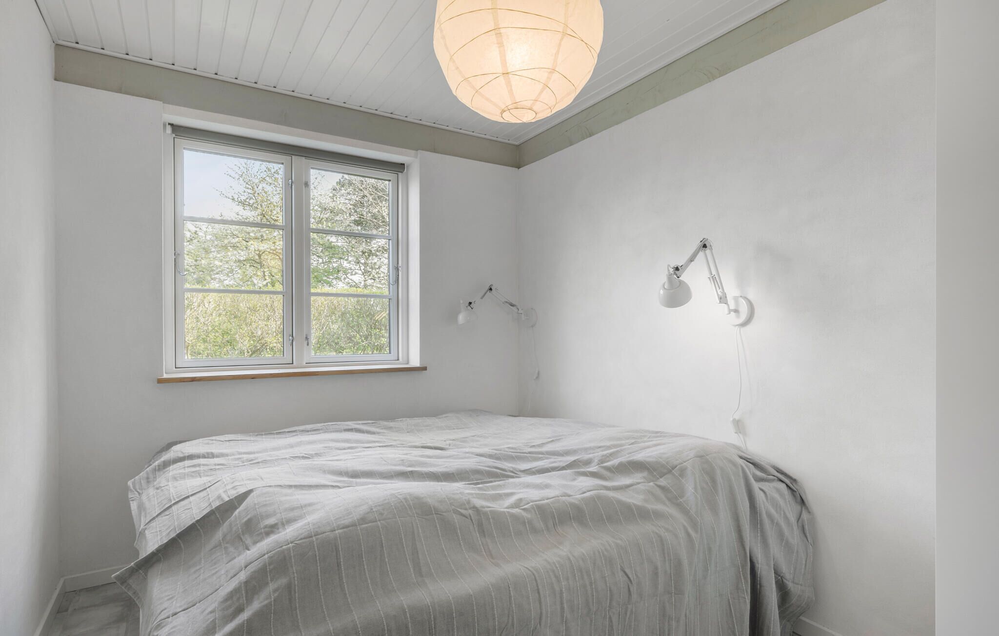 A bedroom with a bed, a window, and a wall-mounted lamp.