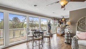 A spacious room with large windows, a wooden deck, a dining area with chairs and a table, a sofa, and a decorative cabinet. - Welcome to our lake house on the beautiful Hiwassee River! (Calhoun)