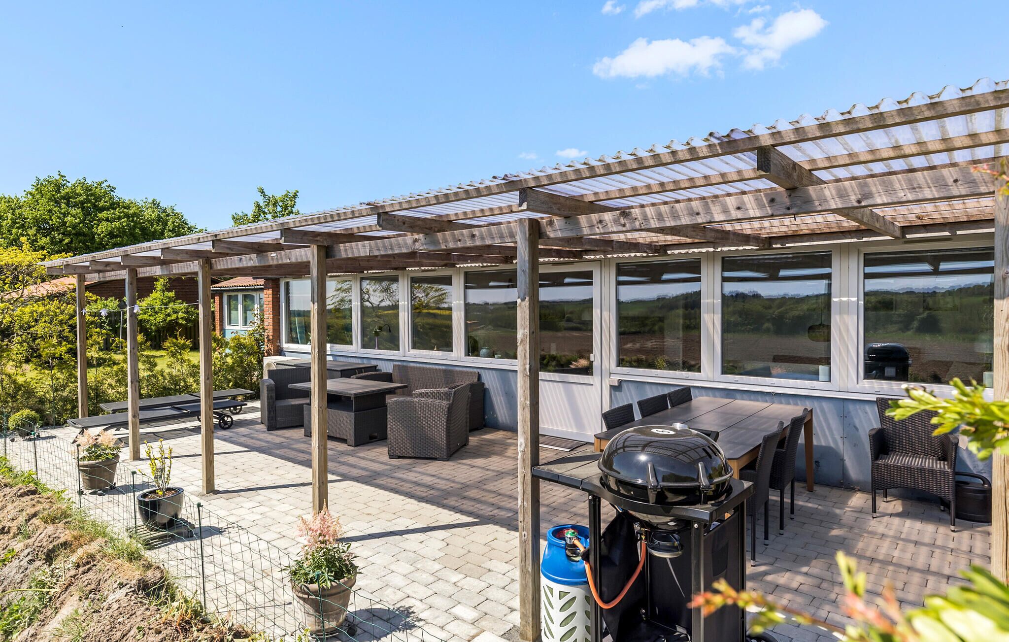 Un patio cubierto con mobiliario exterior, una parrilla y vistas al campo.