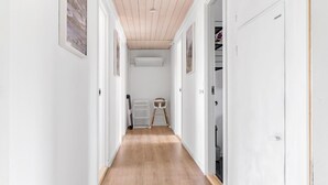 A narrow hallway with wooden flooring, white walls, and a ceiling with wooden beams. There is a baby changing station with a high chair and storage drawers. - 3 bedroom beautiful home in Rønne (Rønne)