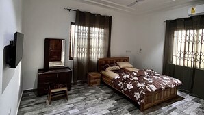 Un dormitorio con cama, cómoda, tocador, ventilador de techo y televisor montado en la pared.
