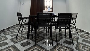 Una habitación con una mesa de comedor y sillas, un ventilador de techo, una lámpara de araña y una ventana con cortinas.