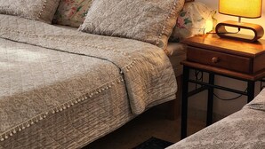 Un dormitorio con cama, almohadas, una mesita de noche con lámpara y otro mueble auxiliar.