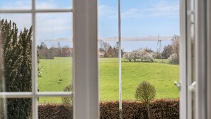 Blick durch ein Fenster auf ein grünes Feld, Bäume und ein entferntes Gewässer.