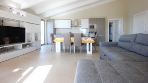 A modern living room with a grey sofa, a flat-screen TV, and a dining area with a table and chairs. - Amazing home in Laureana Cilento (Laureana Cilento)