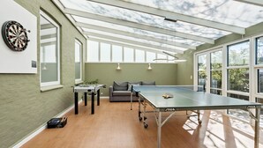 A room with a ping pong table, a dartboard, and a sofa.