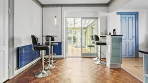 A modern kitchen with a blue door, a dining area with bar stools, and a view through a glass door to an outdoor patio.