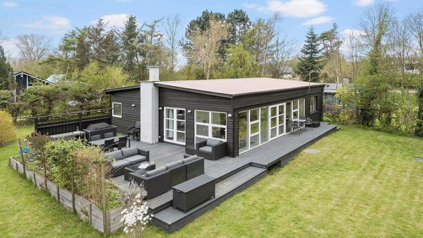 Ein modernes Haus mit Terrasse, Sitzgelegenheit im Freien und einem großen Fensterfront.