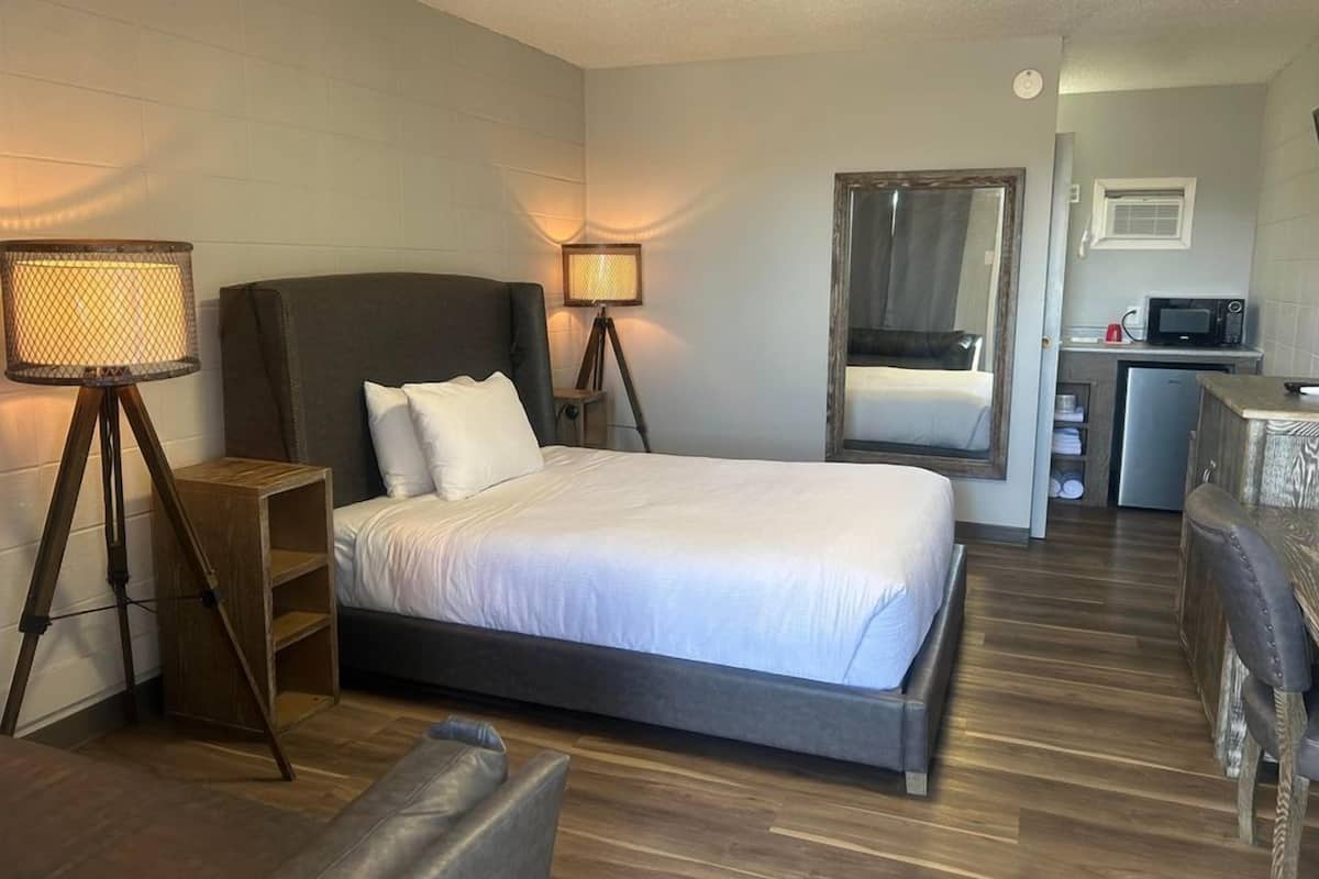 A hotel room with a bed, bedside lamps, a small desk with a microwave, and a mirror.