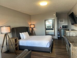 Habitación de hotel con cama, lámparas de noche, escritorio, televisor y kitchenette.