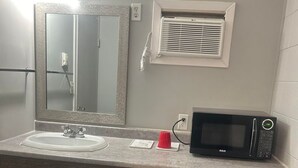 A bathroom with a sink, mirror, microwave, and a small refrigerator. - PARKSIDE INN (Grande Prairie)