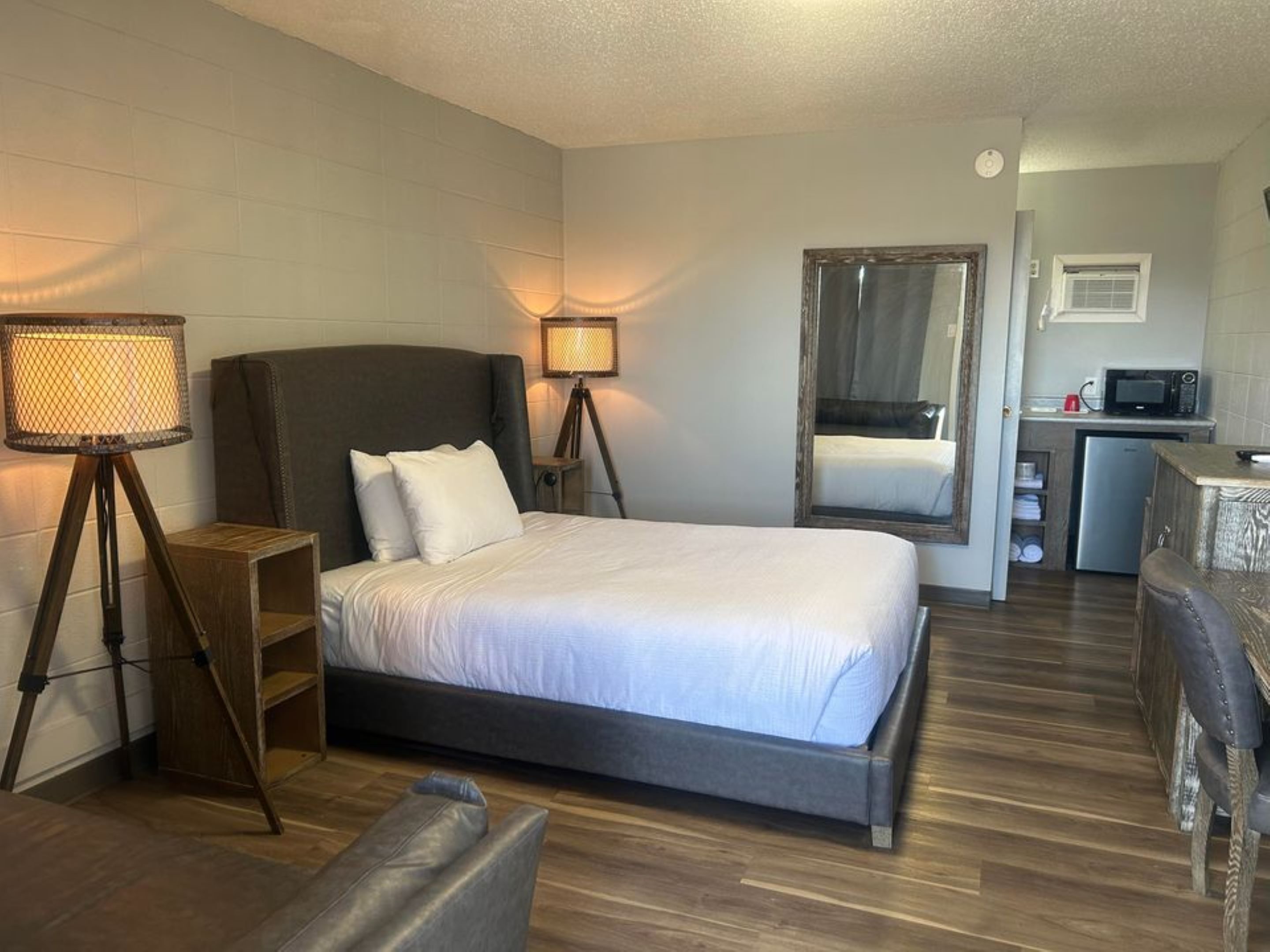Habitación de hotel con cama individual, lámparas de noche, un escritorio pequeño con silla, microondas y refrigerador.