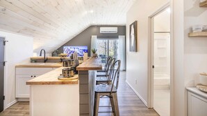 Una cocina moderna con techo de madera, una isla central con taburetes de bar y un televisor en la pared.